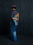 Back view of woman wearing luxury ombre silk  maxy dress and indigo silkchiffon scarf against a dark background.