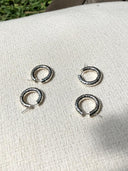 Four Silver Baby Hoop earrings by Rimmba, featuring a hammered beaten design, are displayed on woven fabric in sunlight, with green grass at the top edge. Ethically crafted from 925 Sterling Silver by Rimmba | Sustainable Clothing.