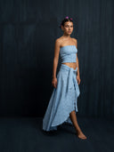 Barefoot woman wearing a baby indigo cotton embroidery strapless top and maxi cotton wrap skirt with a dark background.