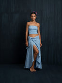 Barefoot woman wearing Suzi's cotton embroidery wrap skirt baby indigo and strapless top botanical dyed. Featuring a slit in the front against a dark background.