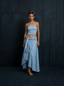 .Barefoot woman wearing Suzi's cotton embroidery wrap skirt baby indigo and strapless top botanical dyed against a dark backgrund.