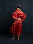 Back view of a barefoot woman wearing Mulberry silk red-ecoprin kimono. Her bun hairstyle with purple flower. Hancrafted botanical-dyed kimono for sustainable luxury fashion and resort wear.