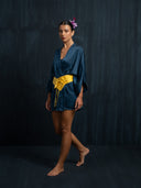 Barefoot woman wearing an indigo mulberry silk kimono above the knee and yellow silk belt against a dark background.