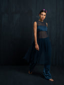 woman wearing an indigo silk chiffon blouse and matching colour silk long pants against a dark background.