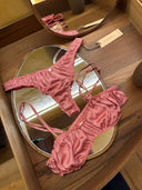 A pink Silk Intimate Set - Bra & Underwear by Rimmba | Sustainable Clothing, featuring ruched details and hypoallergenic fabric, is displayed on a wooden tray with a mirror. A Rimmba brand tag is placed to the right of the set.