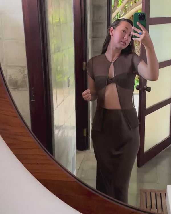 A mirror video indoors of Karunia Fischer's wearing Alila Silchiffon Blouse iron mud with a small front cut-out and matching skirt.