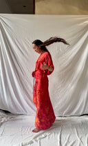 A person twirls gracefully, wearing the Bellas Red Silk Kaftan by Rimmba, their long hair flowing as they stand barefoot on a white cloth against a white fabric backdrop.
